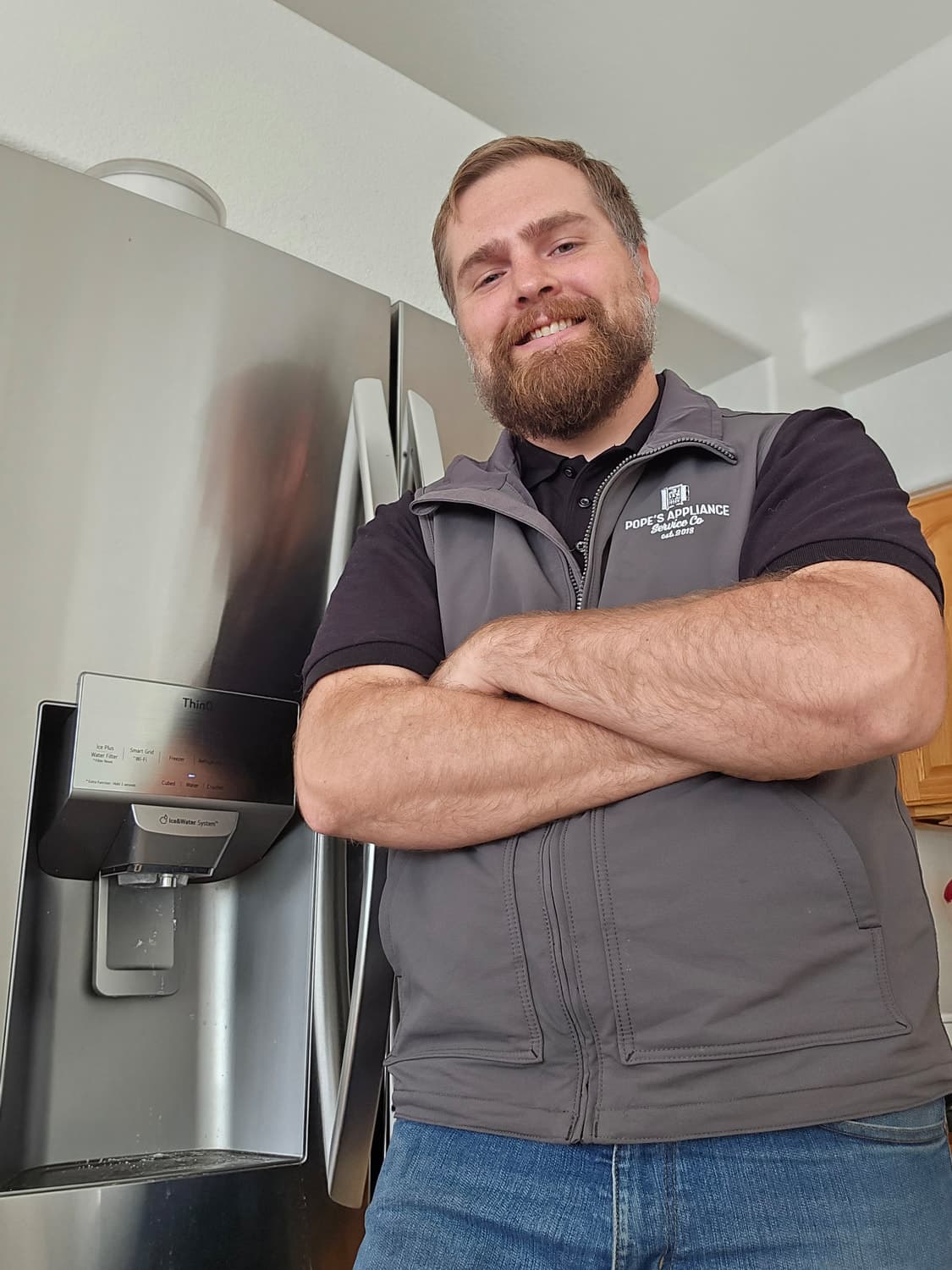 Jonathan Pope in his Pope's Appliance vest, arms crossed, in front of a stainless refrigerator